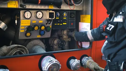 A firefighter in gear adjusting controls on a fire engine during an emergency response.