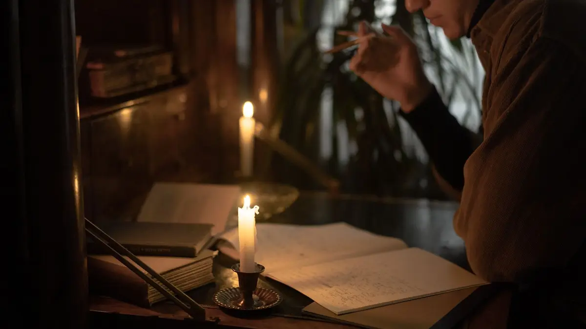 A person reads and writes by candlelight, creating a moody and contemplative atmosphere.