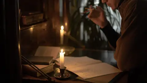 A person reads and writes by candlelight, creating a moody and contemplative atmosphere.