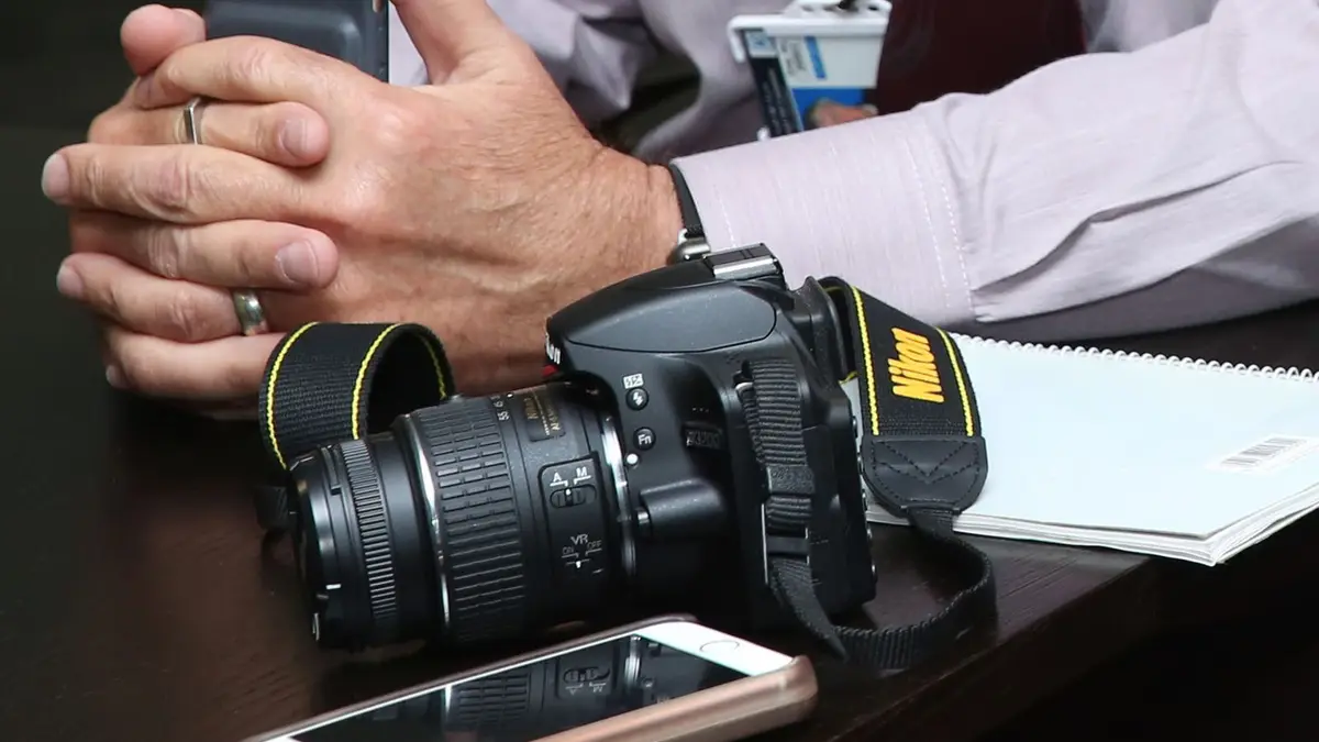 Close-up of a workspace featuring camera equipment, smartphone, and notebook on a table.