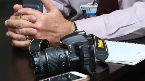 Close-up of a workspace featuring camera equipment, smartphone, and notebook on a table.