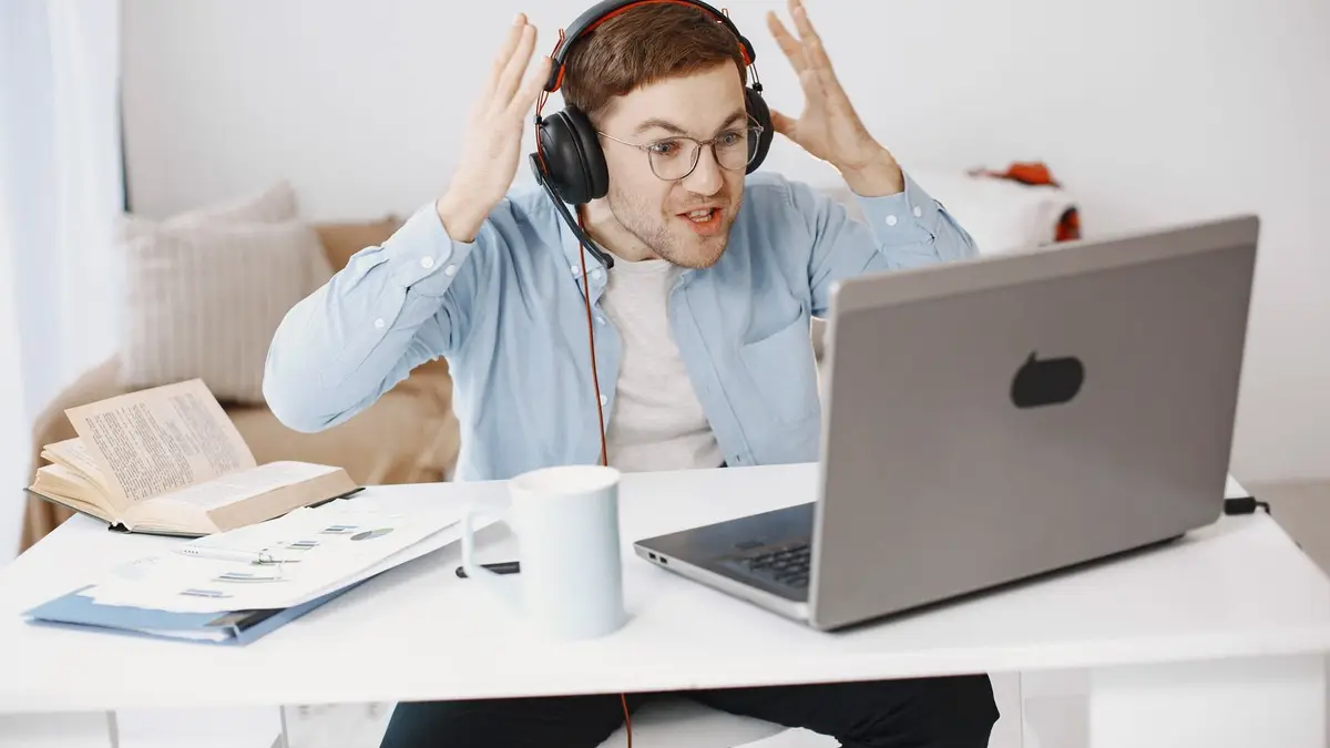 Man expressing frustration with remote work at home desk setup.