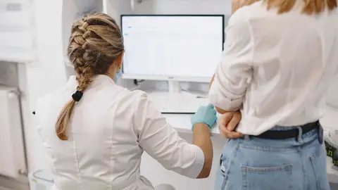 Two healthcare professionals working on a computer in a hospital setting, focused on data analysis.