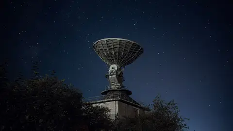 Radio telescope and green lush trees under blue sky with stars at night
