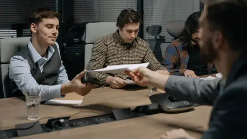 Four professionals exchanging documents during a meeting in an office setting.