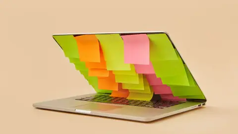A partially closed laptop adorned with assorted colorful sticky notes on the screen.