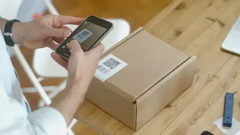 A person uses a smartphone to scan a QR code on a package in an online store setting.
