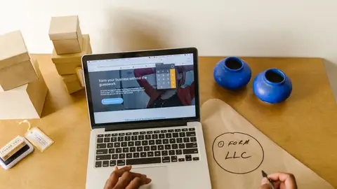 Workspace with laptop, packaging, and handwritten LLC notes, ideal for a small business startup scene.