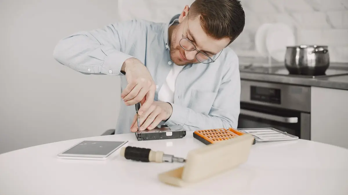 Man wearing glasses using a screwdriver to fix a device on a kitchen table.