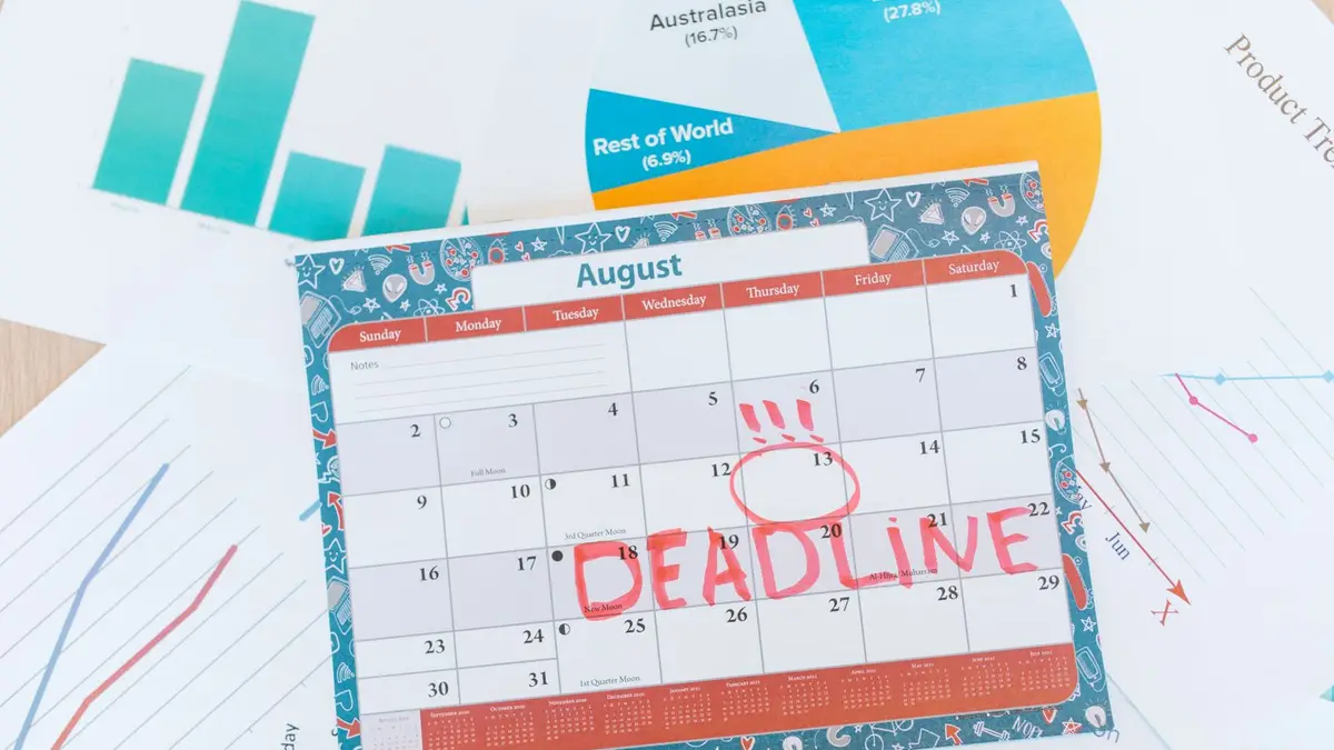 Vibrant August calendar on a desk with deadline marked in red, surrounded by graphs and charts.