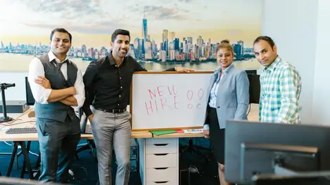 Diverse team standing with 'New Hire' sign, symbolizing collaboration and teamwork.