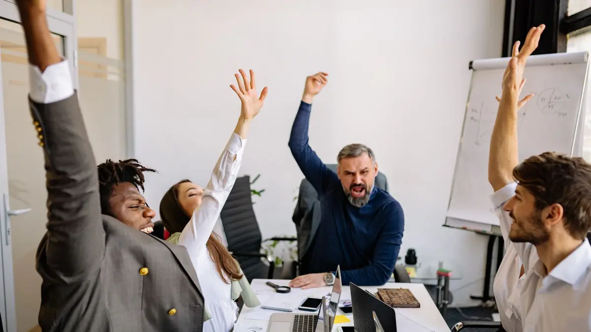 Diverse business team raising hands in excitement during a meeting in a modern office.