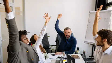 Diverse business team raising hands in excitement during a meeting in a modern office.