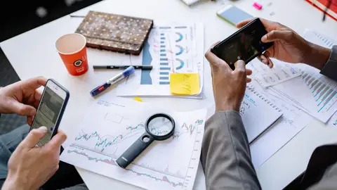 Two professionals analyzing data and graphs with smartphones on a white table.