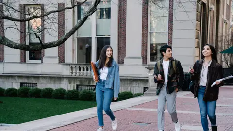Group of young students walking on campus sidewalk on a bright day, showcasing casual university life.