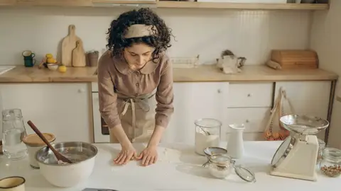A woman preparing dough in a cozy kitchen setting with various baking tools.