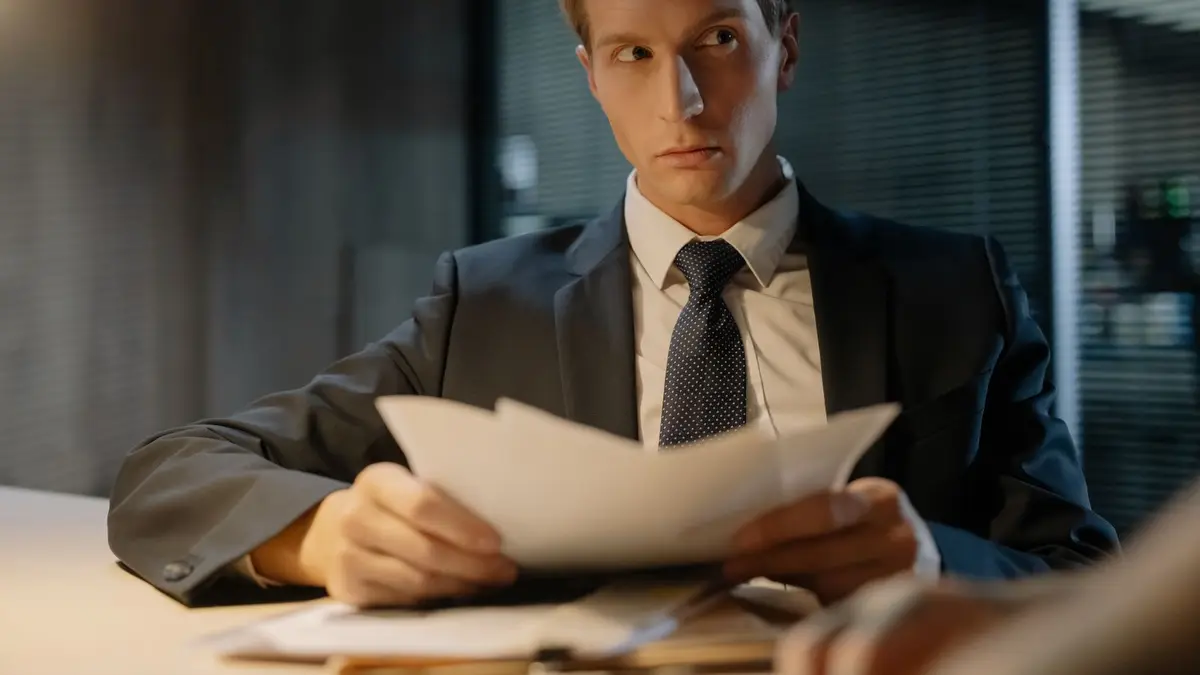 Businessman in suit reviews documents at a desk in a modern office setting.