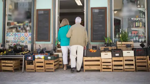 Elderly couple entering a local Portuguese shop surrounded by fresh produce crates.