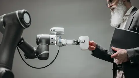 An elderly man receives a cup from a robotic arm in a modern office setting.