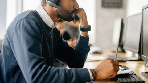 Side view of a bearded man in a headset concentrating at his desk in an office environment.