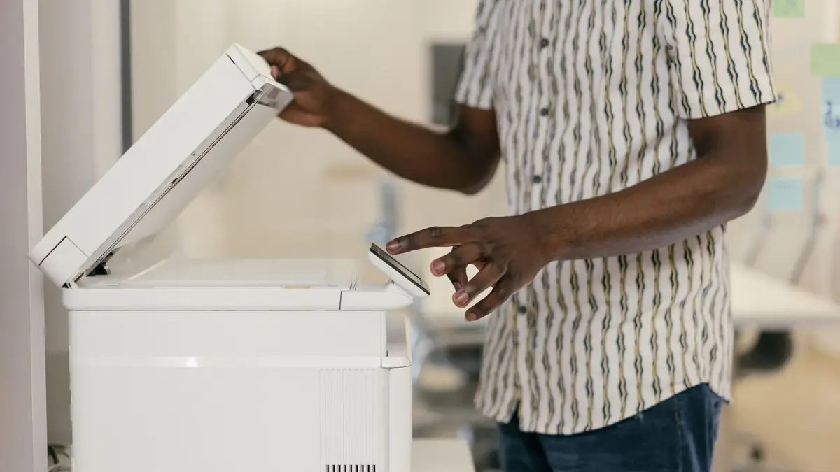 Person operating photocopier in modern office setting, engaging with technology.